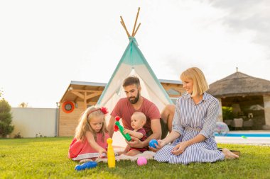 Güzel, genç ve mutlu bir aile, güneşli yaz günlerini arka bahçede kamp yaparak, ebeveynler çocuklarıyla oynayarak geçiriyorlar.