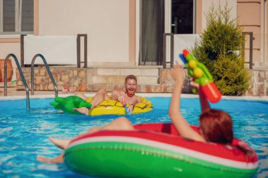 Güzel, genç bir çift havuzda yüzerek ve su sıçratarak eğleniyor, silahlı çatışma yapıyor, yaz tatilinde dinleniyor.