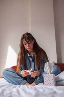 Depresyondaki genç kadın pijama giyiyor, sabahları yatakta oturuyor, gözyaşlarını ve burnunu siliyor ağlarken kağıt mendil kullanıyor.