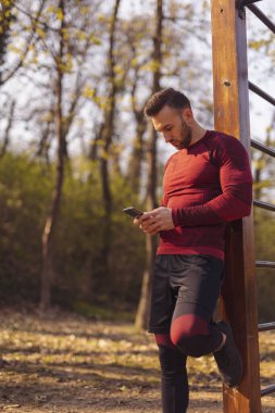 Aktif genç adam spor yaparken akıllı telefon kullanıyor, internette sohbet ediyor ve internette sörf yapıyor.