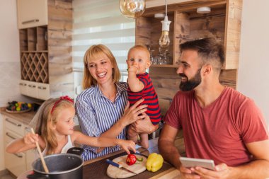 Güzel, mutlu bir aile birlikte yemek pişiriyor, mutfak tezgahında oturuyor ve evde boş vakitlerin tadını çıkarıyor.
