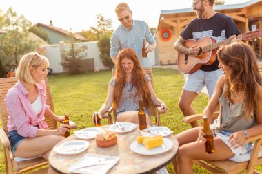 Bir grup arkadaş arka bahçedeki barbekü partisinde gitar çalıp şarkı söyleyerek, bira içerek ve güneşli bir yaz gününde dışarıda dinlenerek eğleniyorlar.