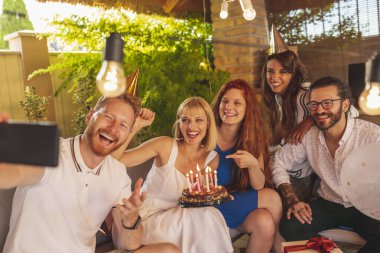 Bir grup neşeli genç arkadaş doğum günü partisinde selfie çekerken eğleniyorlar.