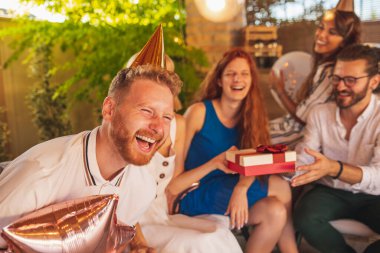 Bir grup neşeli genç, doğum günü kutlaması için toplandı. Arkadaşları, doğum günü kızı hediyelerini açarken eğleniyorlar.