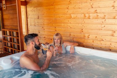 Birbirlerine aşık güzel bir çift otel spa merkezindeki bir jakuzide şarap içip dinleniyor ve tatildeyken eğleniyorlar.