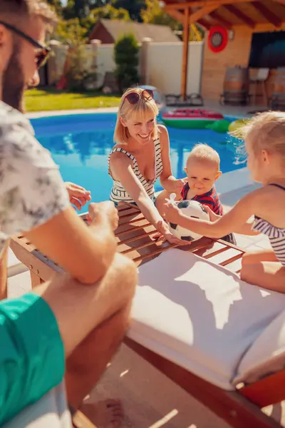 Mother and father having fun playing with their children on a sun bed by the swimming pool, relaxing outdoors on a hot sunny summer day, enjoying summer vacation together