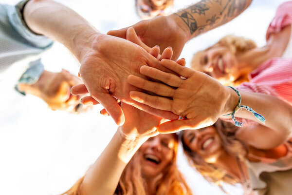 Low angle view of group of cheerful young people gathered together in a circle, looking down to the camera with hands joined in the middle