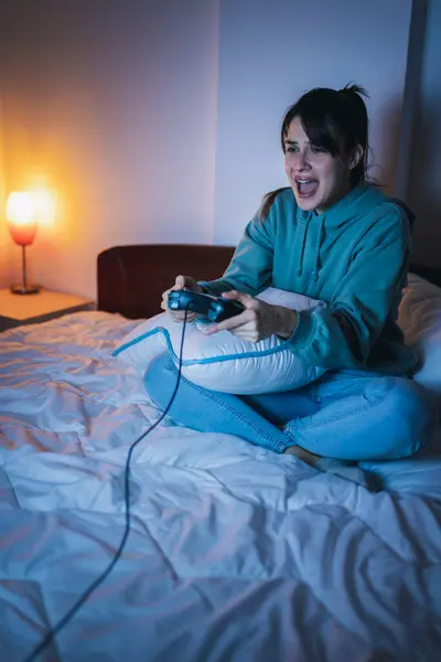 美しい若い女性は 夜にベッドで楽しいゲームをするパジャマを着て 勝つために興奮 — ストック写真