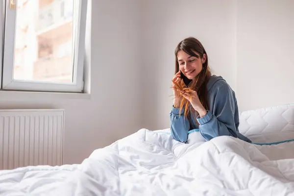 Pijama Giyen Güzel Genç Bir Kadın Yatakta Oturmuş Telefonla Konuşuyor — Stok fotoğraf