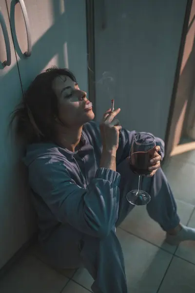 暗闇の中で床に座り ワインを飲んでタバコを吸い 動揺して絶望する抑圧された若い女性 — ストック写真