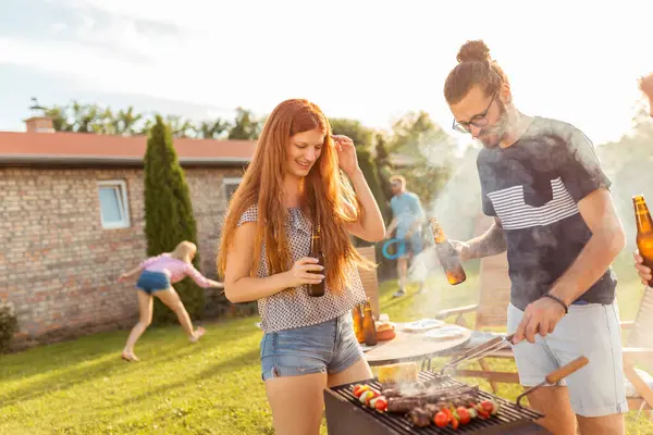 一群快乐的年轻朋友在后院举行烧烤派对 喝啤酒 打羽毛球 在阳光灿烂的夏日户外放松身心 — 图库照片
