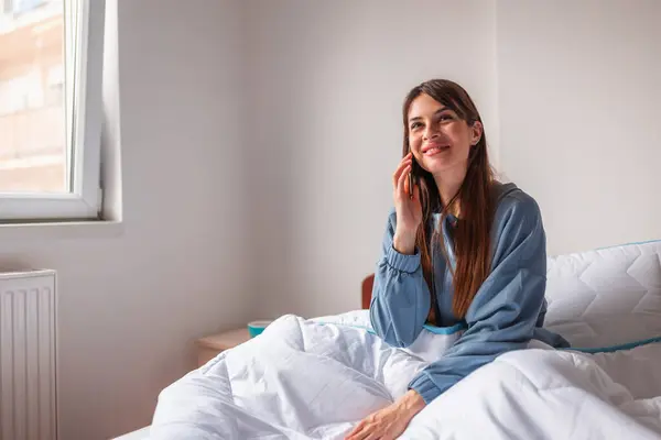 Pijama Giyen Güzel Genç Bir Kadın Yatakta Oturmuş Telefonla Konuşuyor — Stok fotoğraf
