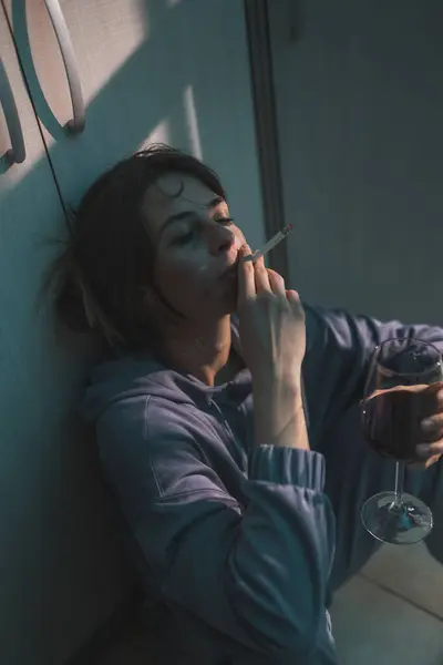 暗闇の中で床に座り ワインを飲んでタバコを吸い 動揺して絶望する抑圧された女性 — ストック写真