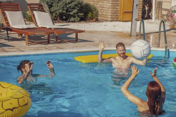 Bir grup arkadaş sıcak bir yaz gününde dışarıda eğleniyorlar, yüzme havuzunda voleybol oynuyorlar, yaz tatilinde dinleniyorlar.