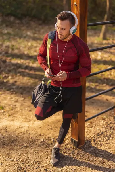 在户外运动前 积极的年轻人头戴耳机提着健身袋听音乐 — 图库照片