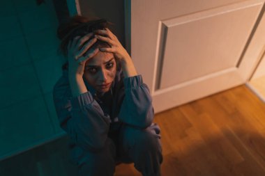 Yüzü makyajla kaplanmış, el ele tutuşmuş ve ağlayan depresif kadının yüksek açılı görüntüsü.