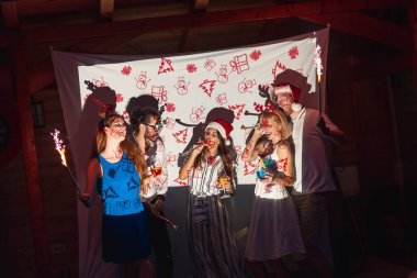 Bir grup arkadaş yeni yıl partisinde eğleniyor, parti ıslıkları çalıyor ve gece yarısı havai fişeklerle el sallıyorlar.