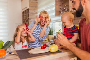 Güzel anne ve kız mutfakta yemek pişirirken eğleniyorlar, bardakta dolmalık biber parçaları tutuyorlar ve komik suratlar yapıyorlar.