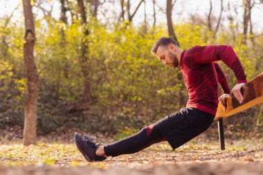 Aktif bir adam güneşli bir sonbahar gününde dışarıda spor yaparken vücut ağırlığı dalışı yapıyor.