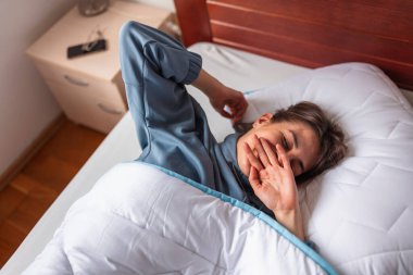 Sabahları pijama giyen, esneyen ve esneyen güzel bir kadının yüksek açılı görüntüsü.