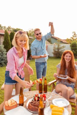 Bir grup genç arkadaş arka bahçedeki barbekü partisinde eğleniyor, açık havada güneşli yaz günlerinin tadını çıkarıyor, bira içiyor, ızgara et yiyor ve dans ediyor.