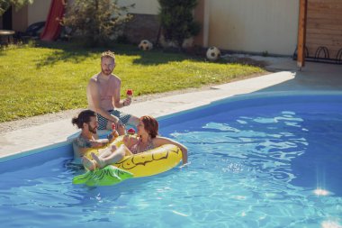 Bir grup genç arkadaş yaz havuz partisinde eğleniyor güneşli yaz günlerini dışarıda geçiriyor ve havuz başında karpuzlu dondurma yiyor.
