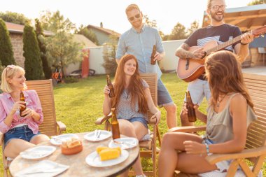 Bir grup arkadaş arka bahçedeki barbekü partisinde gitar çalıp şarkı söyleyerek, bira içerek ve güneşli bir yaz gününde dışarıda dinlenerek eğleniyorlar.