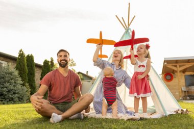 Güzel, genç ve mutlu bir aile, güneşli yaz günlerini arka bahçede kamp yaparak, ebeveynler çocuklarıyla oynayarak, oyuncak uçaklar atarak geçiriyorlar.