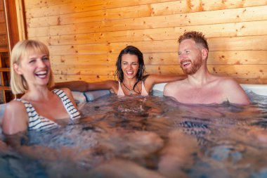 Bir grup neşeli genç arkadaş otel spa merkezindeki jakuzide dinleniyor, tatildeyken eğleniyorlar.