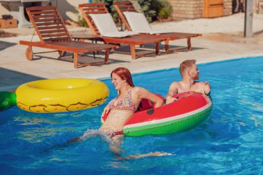 Güzel, genç bir çift havuzda yüzerek ve su sıçratarak eğleniyor, bir havuza tırmanıyor ve zıplıyor, yaz tatilinde dinleniyor.