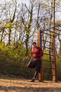 Spor çantası taşıyan, kulaklık takan ve dışarıda antreman yapmadan önce akıllı telefon kullanan genç bir adamın düşük açılı görüntüsü.