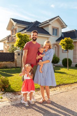 Ebeveynler ve çocuklar yeni evlerinin önünde durup eğleniyorlar. 