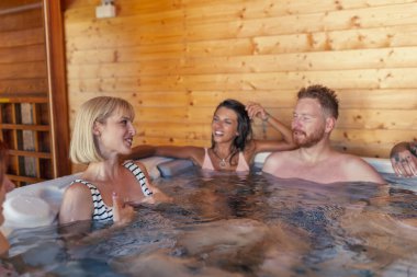 Bir grup neşeli genç arkadaş otel spa merkezindeki jakuzide dinleniyor, tatildeyken eğleniyorlar.