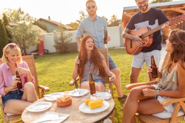 Bir grup arkadaş arka bahçedeki barbekü partisinde gitar çalıp şarkı söyleyerek, bira içerek ve güneşli bir yaz gününde dışarıda dinlenerek eğleniyorlar.