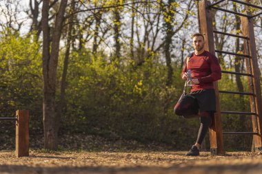 Spor çantası taşıyan atletik bir gencin dar açılı görüntüsü, bir sokak çalışma parkında yapılan yoğun bir idmandan sonra su içmesi.