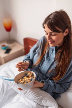 Sabahları pijama giyen güzel genç bir kadın kahvaltıda taze böğürtlenli gevrek yiyor ve evde boş vaktinin tadını çıkarıyor.