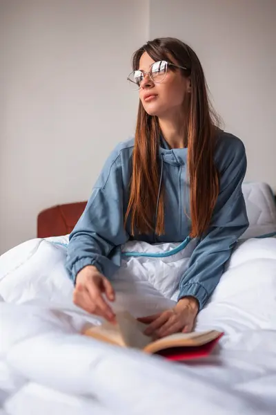 朝ベッドに座ってパジャマを着て 本を読んで自宅でリラックスする美しいペンギンな若い女性 — ストック写真