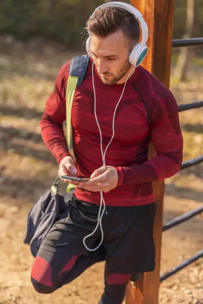 活跃的年轻人头戴耳机 带着健身袋 用智能手机 在户外运动后听音乐 — 图库照片