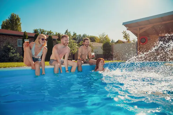 一群快乐的年轻朋友在户外的夏季派对上玩得很开心 他们坐在游泳池边 一边喝啤酒 一边往对方身上泼水 — 图库照片
