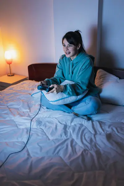 Beautiful young woman wearing pajamas having fun playing video games in bed at night