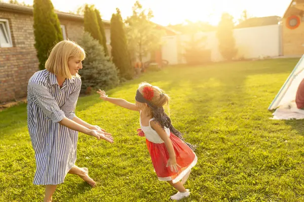 美丽的母亲和女儿在后院度过了一个阳光明媚的夏日 小女孩蒙着眼睛跑来跑去 追逐着妈妈 一边玩着瞎子的把戏 — 图库照片