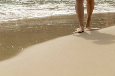 Kumsalda yürüyen bir kadın, çakıl taşlarında ayak izleri bırakıyor.