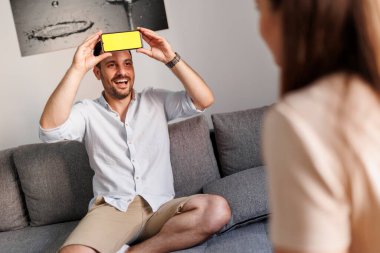 Çift evde kelime tahmin oyunu oynayıp akıllı bir telefon uygulamasından sözcükleri izah edip tahmin ediyor.