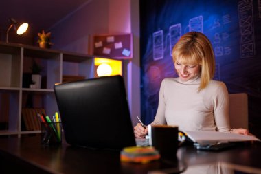 Ofiste fazla mesai yapan bir kadın gece geç saatlere kadar masasında oturuyor evrak işleriyle uğraşıyor ve sözleşmeleri okuyor.