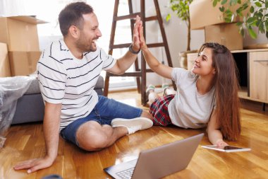 Birbirine aşık güzel genç bir çift birlikte yaşıyor, internette dizüstü bilgisayar ve tablet bilgisayarlarla geziniyor, ev dekorasyonu fikirleri arıyor.