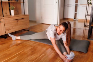 Spor giyim sektöründe aktif genç bir kadın yoga minderine uzanıyor ve antrenman için ısınıyor.