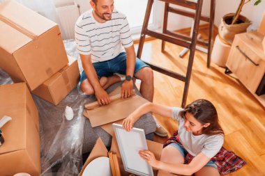 Güzel, genç ve aşık bir çift yeni evlerine taşınırken karton kutulardan bir şeyler çıkarırken eğleniyorlar.