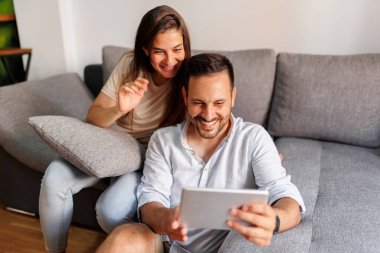 Güzel, genç aşık bir çift evde rahatlıyor, tablet bilgisayar kullanarak internette sörf yapıyor.