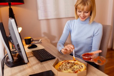 Ofisteki masasında oturan bir kadın öğle yemeği molasında pizza yiyor.