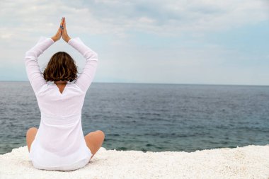 Yunanistan 'ın Thassos adasında, bulutlu bir yaz gününde mermer plajda yoga yapan genç bir kadın.